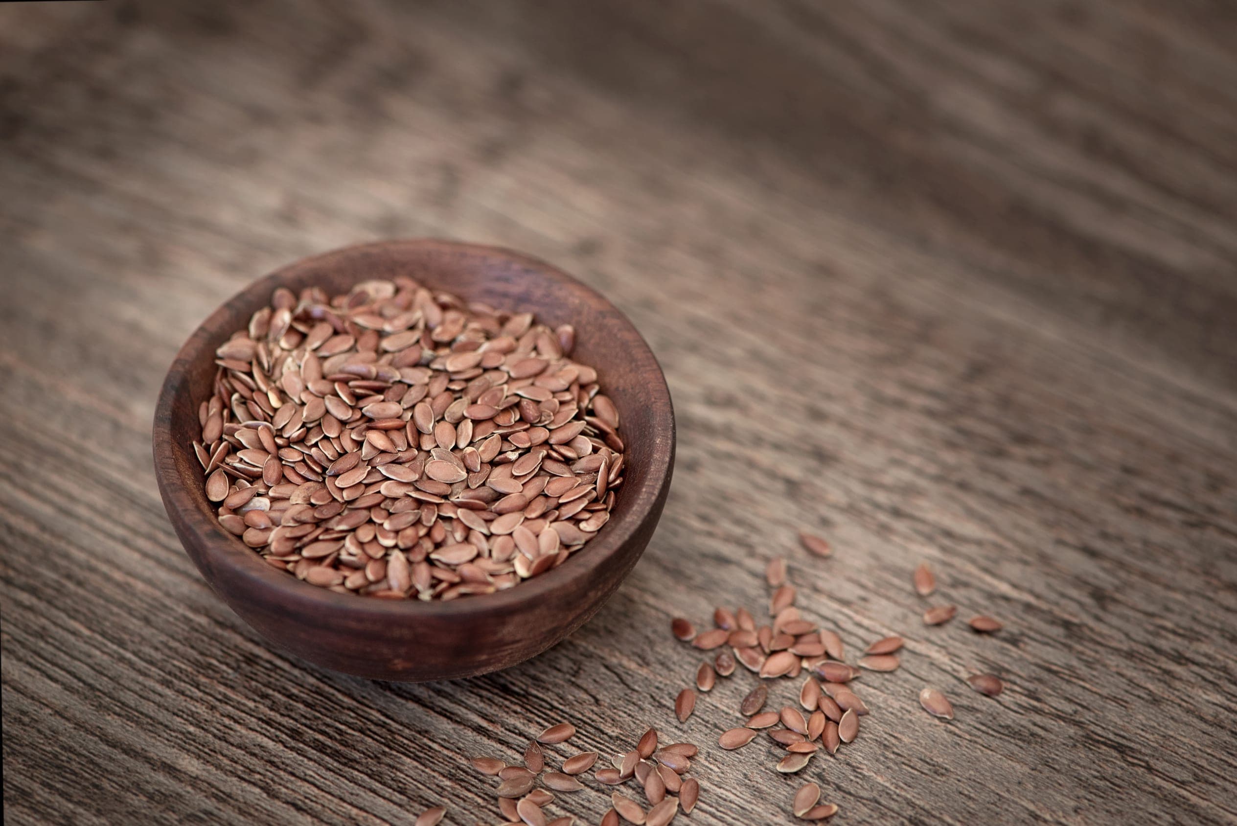 Brown flaxseed in a wooden bowl on a weathered wooden surface